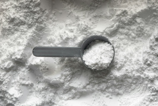 A grey plastic scoop filled with white powder resting on a pile of powder
